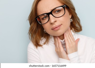 Close up of sick businesswoman in glasses suffering from throat problems, holding hands on her lymph nodes. Thyroid gland, painful swallowing concept. Inflammation of the upper respiratory tract