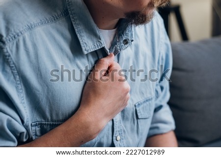 Close up sick man having difficulty breathing pain heart, touches chest with hand sitting on sofa at home. Trouble breathing, chest pain. Heart attack, thoracic osteochondrosis, panic attack concept