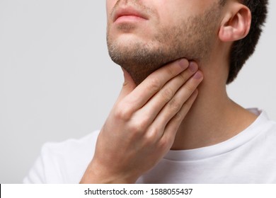 Close up of sick man suffering from throat problems, grey background, isolated. Thyroid gland, painful swallowing, pharyngitis, laryngeal swelling concept. Inflammation of the upper respiratory tract