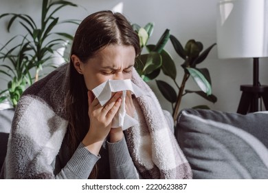 Close up of sick woman sitting on sofa freezing blowing running nose got fever caught cold sneezing in tissue, ill brunette girl covered with blanket, having influenza symptoms coughing at home - Shutterstock ID 2220623887
