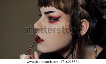 Close up side angle of a goth / punk look teen girl applying dark red lipstick
