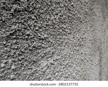 Close up side angle shot of a rough, coarse grey cement concrete wall texture outdoors under natural daylight. 
