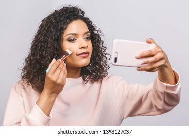 Close Up Side Portrait Of Beautiful Aro American Woman Applying Makeup With Brush. Foundation For Dark Skin. Using Phone. 