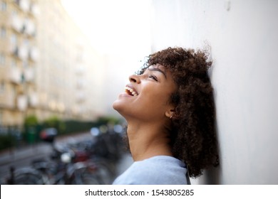 Close up side portrait of beautiful smiling young african american woman leaning against wall outside
