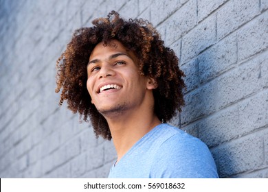 Close up side portrait of cool young man with curly hair smiling against gray wall
