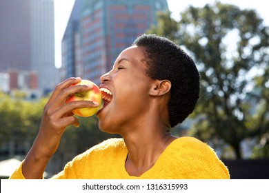 Close Up Side Portrait Of Healthy Young Black Woman Eating Apple Outdoors