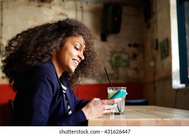 Close Up Side Portrait Of Smiling Young African Lady Relaxing In A Coffee Shop With Mobile Phone