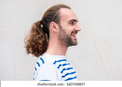 Close Up Side Portrait Of Young Man With Long Hair In Ponytail Smiling By White Background