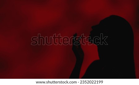 Close up side profile shot of a young woman looking away and raising hand up to her lips gracefully on a dark red background.