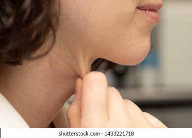 A close up and side profile view of a young Caucasian woman pinching the layer of fat around her neck. Body dysmorphia concept.