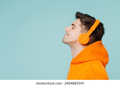 Close up side profile view young man he wearing orange hoody casual clothes listen to music in headphones isolated on plain pastel light blue cyan color background studio portrait. Lifestyle concept - Powered by Shutterstock