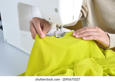 Close up side top view of cropped female hands sewing lime color fabric on professional manufacturing machine at seamstress workplace. Tailor hands holding textile for dress production.  - Powered by Shutterstock