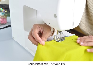 Close up side top view of cropped female hands sewing lime color fabric on professional manufacturing machine at seamstress workplace. Tailor hands holding textile for dress production.  - Powered by Shutterstock