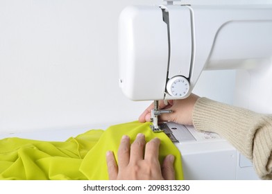 Close up side top view of cropped female hands sewing lime color fabric on professional manufacturing machine at seamstress workplace. Tailor hands holding textile for dress production.  - Powered by Shutterstock