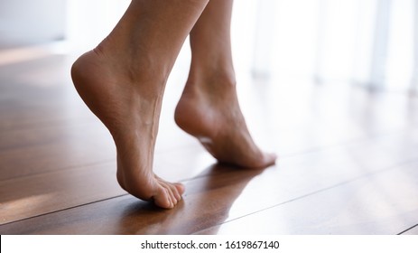 Close up side view beautiful female feet with perfect smooth skin standing tiptoe on warm wooden floor with underfloor heating, barefoot young woman walking at home, enjoying morning, relaxing