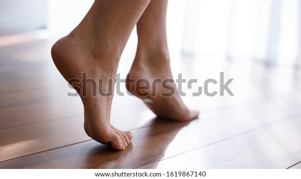 Close up side view beautiful female feet with\
perfect smooth skin standing tiptoe on warm wooden floor with\
underfloor heating, barefoot young woman walking at home, enjoying\
morning, relaxing