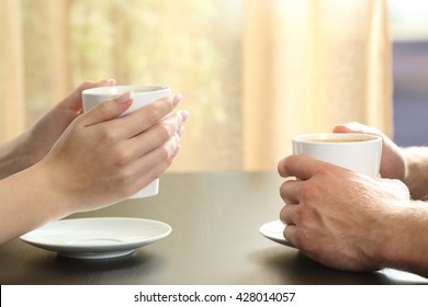 Close Up Of Side View Of A Couple Or Friends Talking With Hands Holding Coffee Cups On A Table With A Window And Curtain In The Background