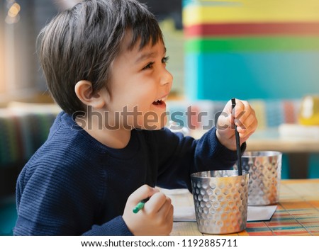 Close up side view of Cute kid sitting on sofa drinking cold drink in restaurant,Toodler drinking soda or soft drink with straw,Child with smilling face sitting on couch and holding straw