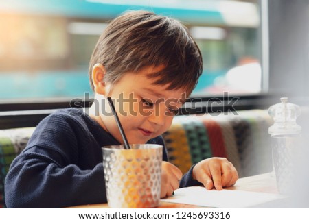 Close up side view of Cute kid sitting on sofa drinking cold drink in restaurant,Toodler drinking soda or soft drink with straw,Child with smilling face drawing or painting on white paper