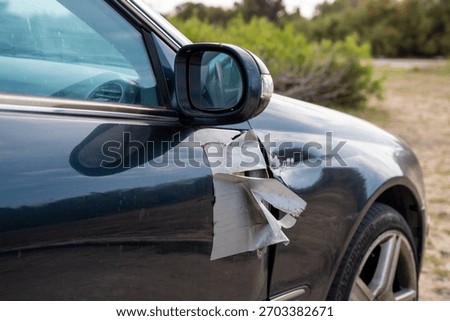 Close side view of a dark blue car with a taped broken mirror and visible dent near front wheel