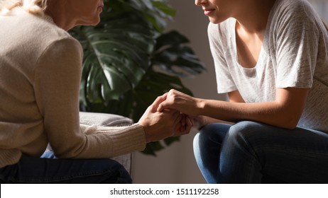 Close up side view of elderly mother and grownup daughter sit at home talk giving advice, loving senior mom and adult offspring child hold hands having intimate close moment, show support and empathy