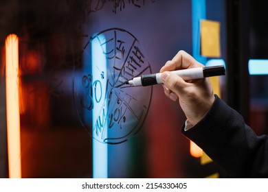 Close Up Side View Of Male Hand Drawing A Pie Marketing Chart On Glass Office Board With A Black Marker. Finance, Budget, Project Planning Strategy. Scrum Kanban Board With Sticky Notes