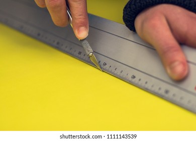 Close up side view of a man cutting precisely through yellow plotter foil used for industrial design with a sharp cutter knife, a ruler and his bare hands