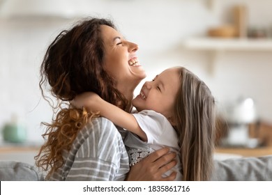 Close up side view overjoyed smiling young mother and daughter hugging and laughing, enjoying tender moment, happy mum and adorable preschool girl kid cuddling, having fun together at home - Shutterstock ID 1835861716