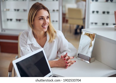 Close up side view portrait of blonde Caucasian business woman in white shirt sitting at the table with laptop and looking away in room indoors - Shutterstock ID 1902533704