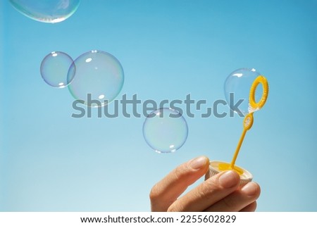 Close up side view shot of young man blowing soap bubbles on blue background. Focus on hands and wand.