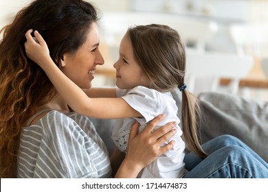 Close Up Side View Smiling Little Girl Running Hands Through Mom S Hair, Showing Love Tenderness. Happy Young Woman Enjoying Sweet Lovely Family Moment With Child Daughter At Home, Looking Into Eyes.