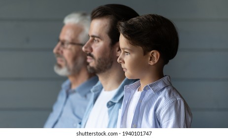Close up side view of three generations of Caucasian men stand in row look in distance show unity and family support. Small boy with young father and older grandfather reunited. Offspring concept. - Shutterstock ID 1940101747