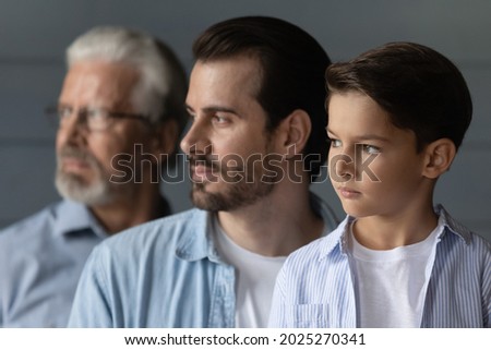 Close up side view of three generations of Caucasian men isolated on grey wall background look in distance thinking. Little teen boy child with young father and old grandfather show family unity.