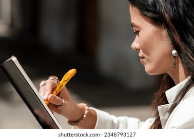 Close side view woman writing diary outdoors  She is wearing jewelry   using an orange pen  Traditional creativity  non  technology concept 