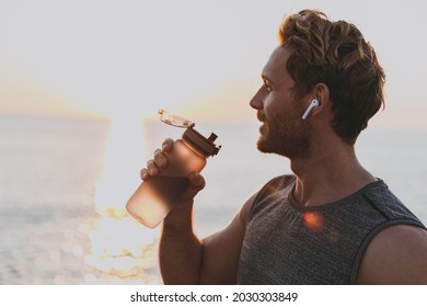 Close Up Side View Young Sporty Toned Fit Sportsman Man 20s Wearing Sport Clothes Earphones Warm Up Train Drink Water At Sunrise Sun Dawn Over Sea Beach Outdoor On Pier Seaside In Summer Day Morning