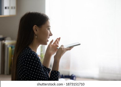 Close Up Side View Young Woman Recording Voice Message, Holding Phone Near Mouth, Sitting At Desk At Home, Chatting Online, Making Call, Talking By Speakerphone, Activating Assistant On Smartphone