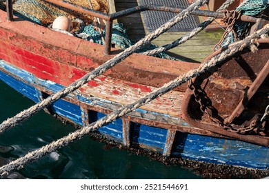 Close up of side of a weathered red and blue colored wooden fishing boat with rusted metal elements, fishing nets and hull full of (quagga or zebra) mussels above and under the water line - Powered by Shutterstock