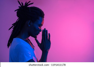 Close up of silhouette African man with dreadlocks praying on purple background