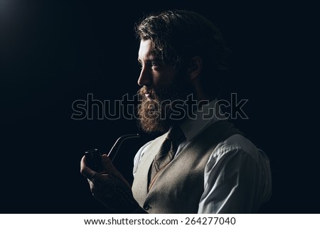 Close up Silhouette Man with Long Goatee Beard Holding a Smoking Pipe While Looking to the Left of the Frame on a Black Background.