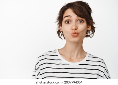 Close Up Of Silly And Cute Brunette Girl Pucker Lips, Funny Kissing Face, Looking Coy At Camera, Standing In T-shirt Against White Background.