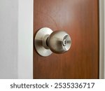 Close up silver handle knob with wooden door and white wall background.