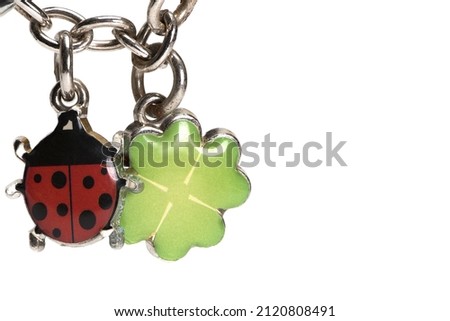 Close up of silver metal chain with two small lucky charms on it a ladybug and a four leaf clover made of silver on white background