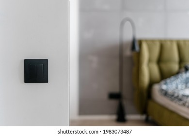 Close up of simple black matte light switch on white wall with bed and metal standing lamp in the blurred background, electrical system in stylish minimalistic loft style bedroom at home - Shutterstock ID 1983073487
