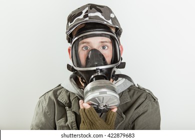 Close Up Of Single Male Teen In Jacket, Brown Gloves And Gray Camouflage Hat Holding A Fire Fighter Respirator Gas Mask On His Face