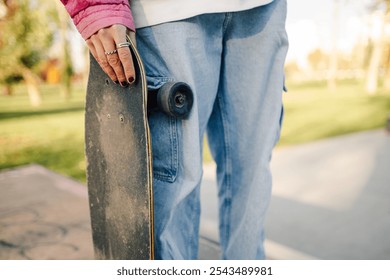 Close up of a skater holding a well worn skateboard at a skatepark, ready for action on a sunny day, showcasing a passion for skateboarding and urban sports - Powered by Shutterstock