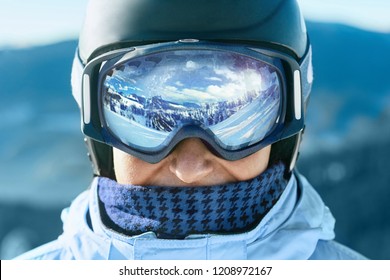 Близко к лыжным очки человека с отражением заснеженных гор. Горный хребет отражается в лыжной маске. Портрет человека на горнолыжном курорте на фоне гор и неба