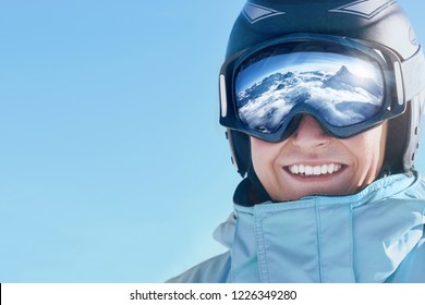 Close Up Of The Ski Goggles Of A Man With The Reflection Of Snowed Mountains.  A Mountain Range Reflected In The Ski Mask.  Portrait Of Man At The Ski Resort.  Wearing Ski Glasses. Winter Sports. 