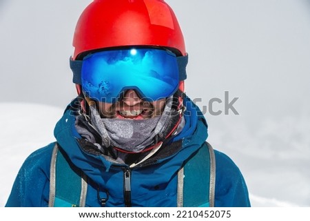 Close up of the ski goggles of a man with the reflection of snowed mountains. A mountain range reflected in the ski mask. Portrait of man at the ski resort on the background of mountains and sky