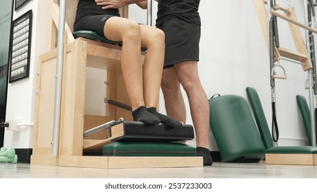 Close up of skilled instructor guiding student Pilates leg press on Wunda Chair equipment. Trainer seated leg press pose for engaging core stability and improving lower body. Focus on leg. Habituate. - Powered by Shutterstock