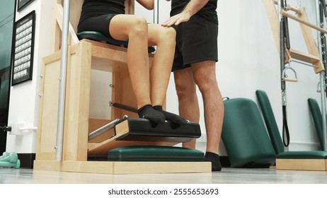 Close up of skilled instructor guiding student Pilates leg press on Wunda Chair equipment. Trainer seated leg press pose for engaging core stability and improving lower body. Focus on leg. Habituate. - Powered by Shutterstock